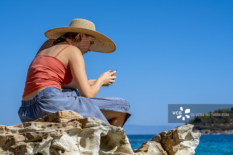 希腊拉戈尼西海滩风蚀岩石旁玩手机女孩图片素材
