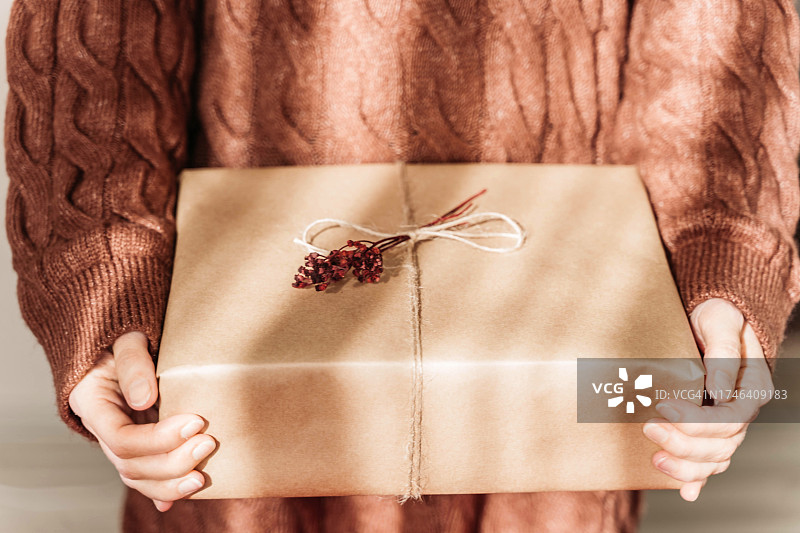 手持红色干花牛皮纸圣诞礼物，针织毛衣背景，特写图片素材