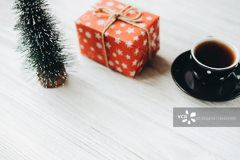 红色礼品盒、玩具圣诞树、白色木质表面的咖啡杯图片素材