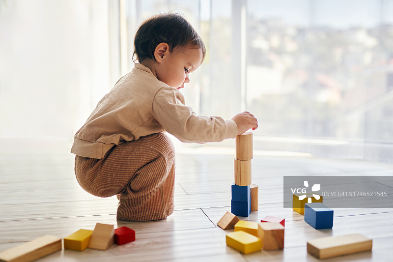女孩在地板上玩木头积木图片素材