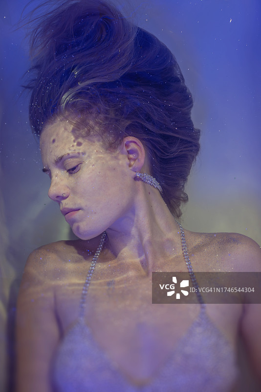 年轻漂亮的女人在彩色光线下，在蕾丝面纱下的水中图片素材