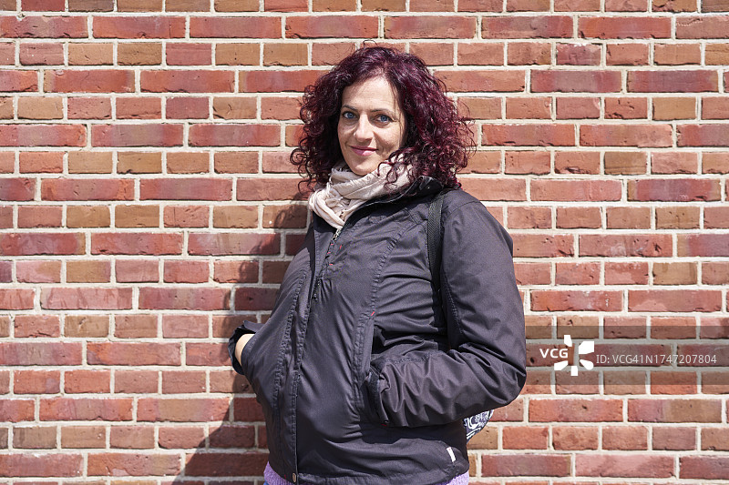 美丽的女人：站在砖墙前微笑，身穿外套和围巾图片素材