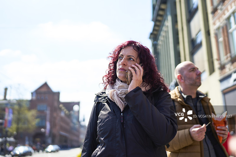 在街边人行道上打电话的女游客和她旁边的男人（正面视角）图片素材