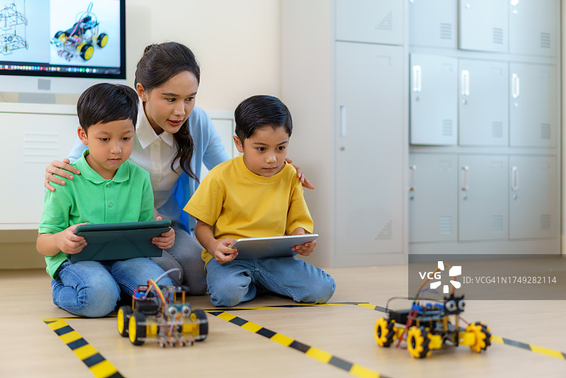 在机器人组装课上参加机器人汽车比赛的亚洲男孩，老师正在指导图片素材