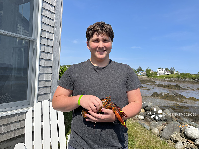 手持刚捕获的龙虾的微笑少年图片素材