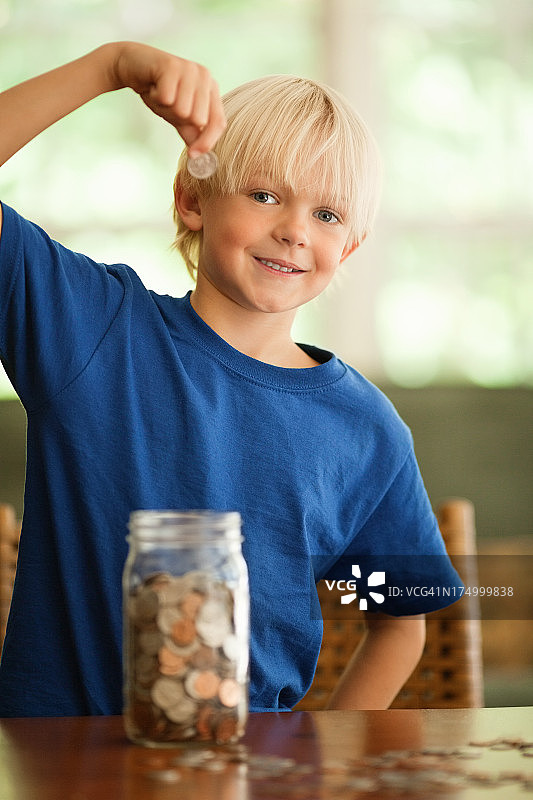 小男孩往玻璃罐里存钱图片素材