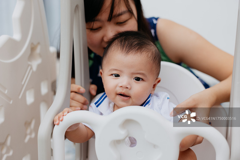 快乐的母亲在婴儿秋千上推着她的男婴图片素材