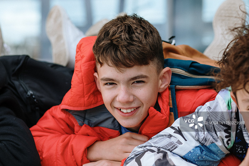 快乐的少年穿着鲜红色的夹克与同学在长椅上休息图片素材