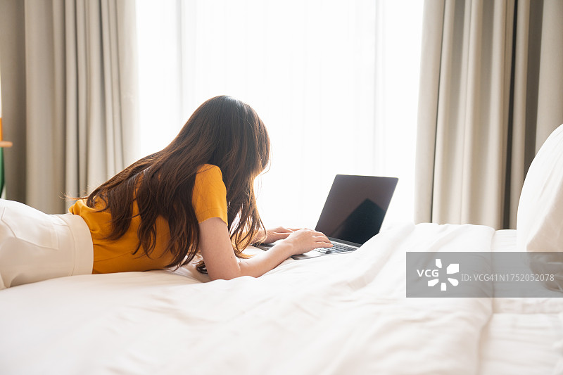 在卧室里放松时使用笔记本电脑的快乐年轻女孩图片素材