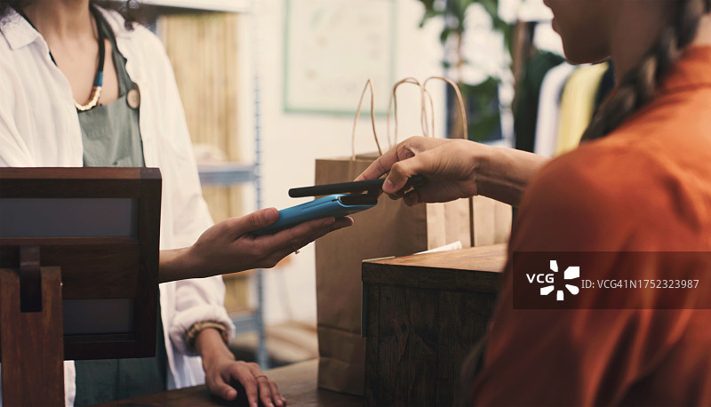 收银员、顾客和带有POS机的手机，商店或小型零售企业的金融科技或数字支付。人物、手和服装销售员，移动应用程序上的销售点，点击和购物袋图片素材