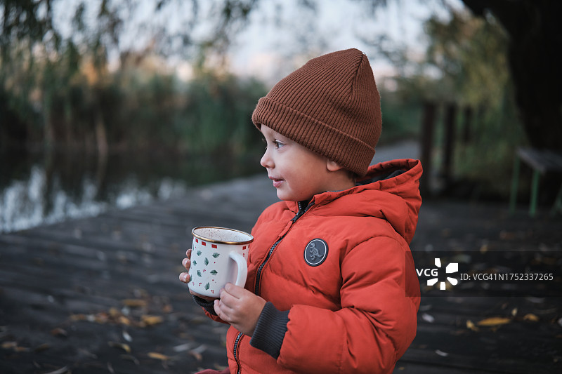 和孩子一起露营：学龄前儿童在秋季大自然中拿着旅行杯喝热饮图片素材