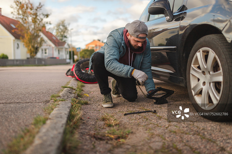年轻男子使用千斤顶在户外抬起汽车更换轮胎图片素材