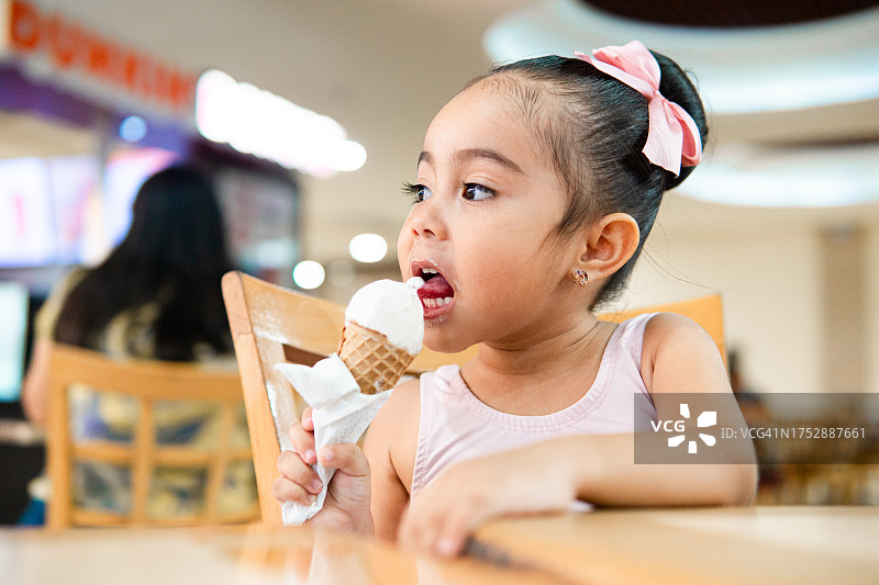 在购物中心吃香草冰淇淋的西班牙裔小女孩图片素材