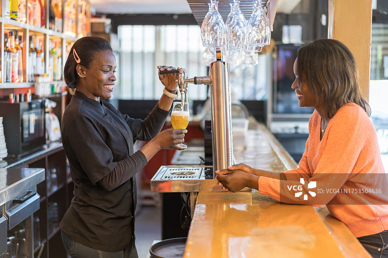 女人在酒吧工作时从水龙头倒啤酒到玻璃杯中图片素材
