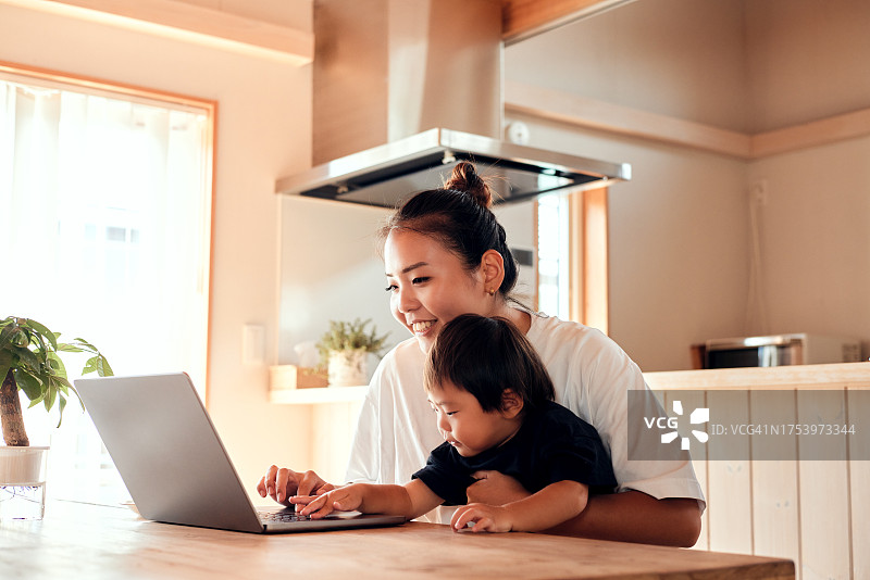 母亲在家购物，让儿子坐在腿上用笔记本电脑图片素材