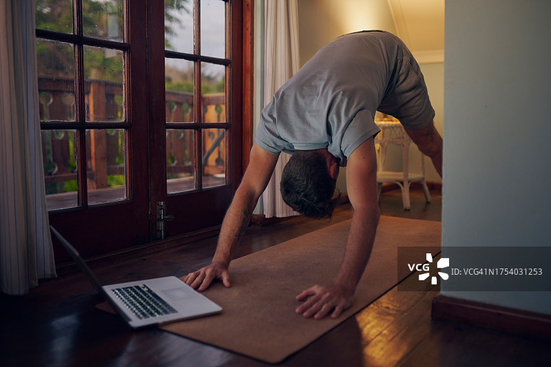 男人在家用笔记本电脑上做瑜伽和伸展运动，用于家庭训练、健身和整体健康，虚拟课程或视频流。人在普拉提锻炼，运动和平衡，在电脑上获得禅意与平静图片素材