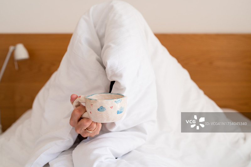 年长男人裹着被子在床上喝茶，手部特写图片素材