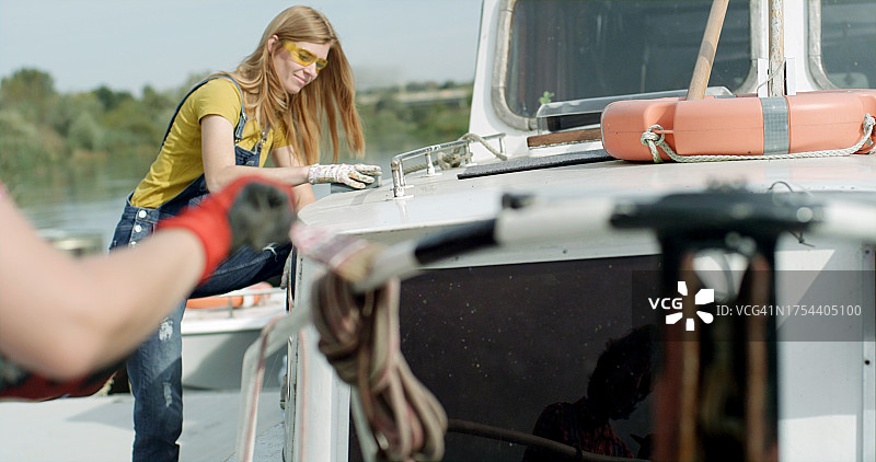 两名女子正在翻新一艘生锈的旧船。她们粉刷并清理铁锈。粉刷扶手。DIY项目。图片素材