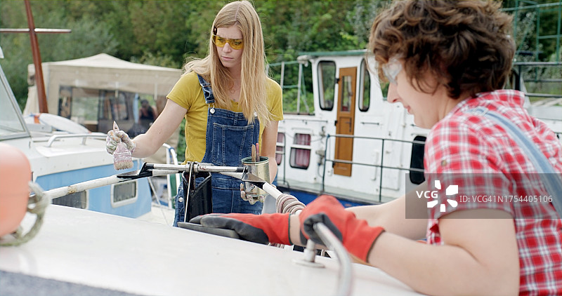 两名正在翻新一艘生锈旧船的女人。她们正在油漆和清理铁锈。（DIY项目）图片素材
