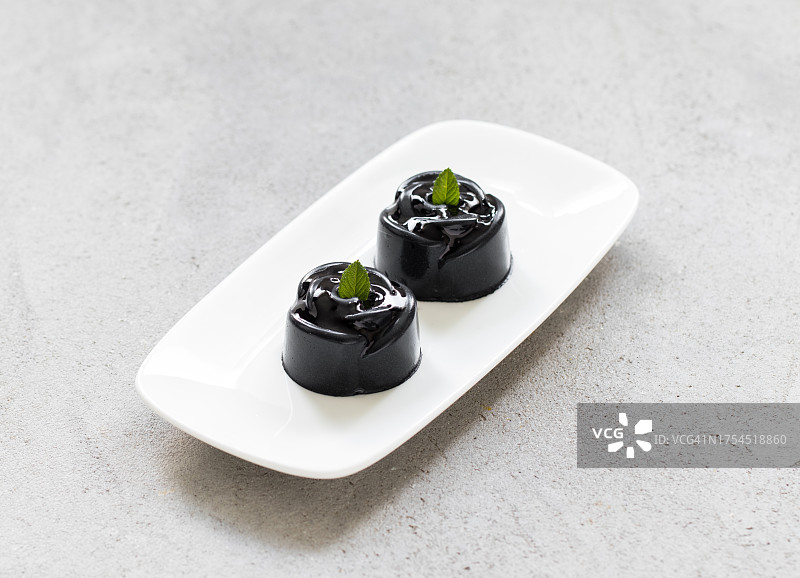 两款黑色抹茶奶油迷你玫瑰甜点，配有酱汁，置于盘中，添加竹炭粉。浅灰色背景，特写图片素材