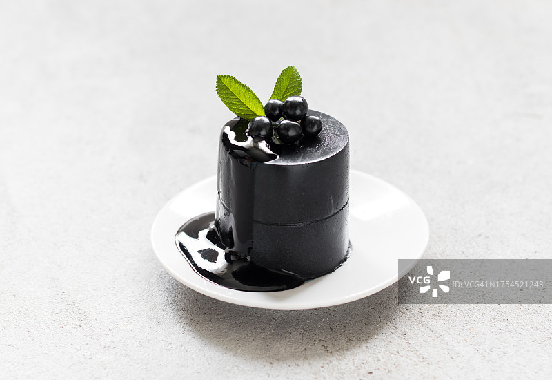意大利黑抹茶奶油果冻甜点，意式奶冻，配酱汁，盘装，饰以黑色浆果，浅灰色背景，特写图片素材