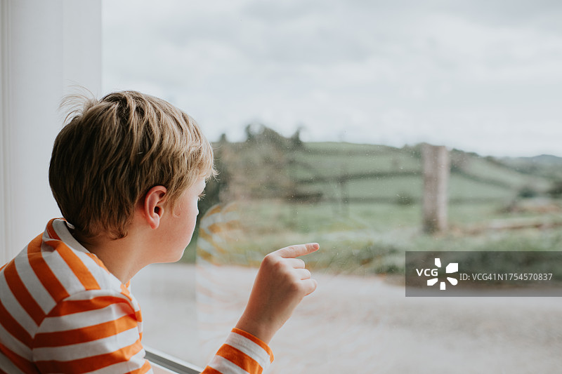 小男孩看着窗外，用手指触摸玻璃图片素材