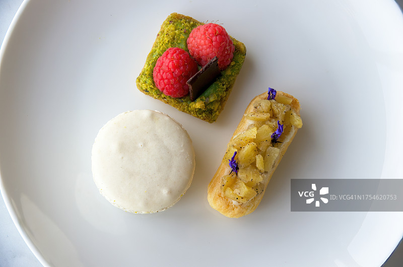 迷你法式糕点拼盘：菠萝薰衣草泡芙、香草马卡龙、覆盆子开心果巧克力切片图片素材