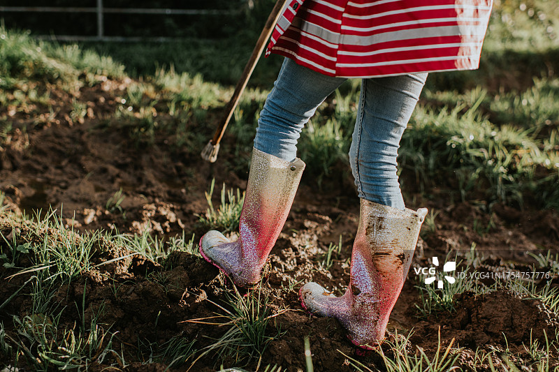 特写：孩子穿着闪光威灵顿靴在泥泞的田野里行走图片素材