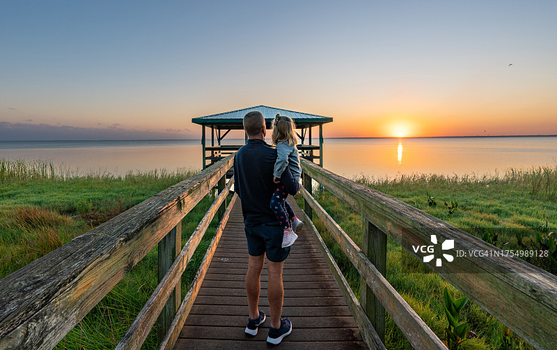 父亲和女儿在佛罗里达州中部奥兰多附近的阿波普卡湖木板路和码头上欣赏充满活力的日出图片素材