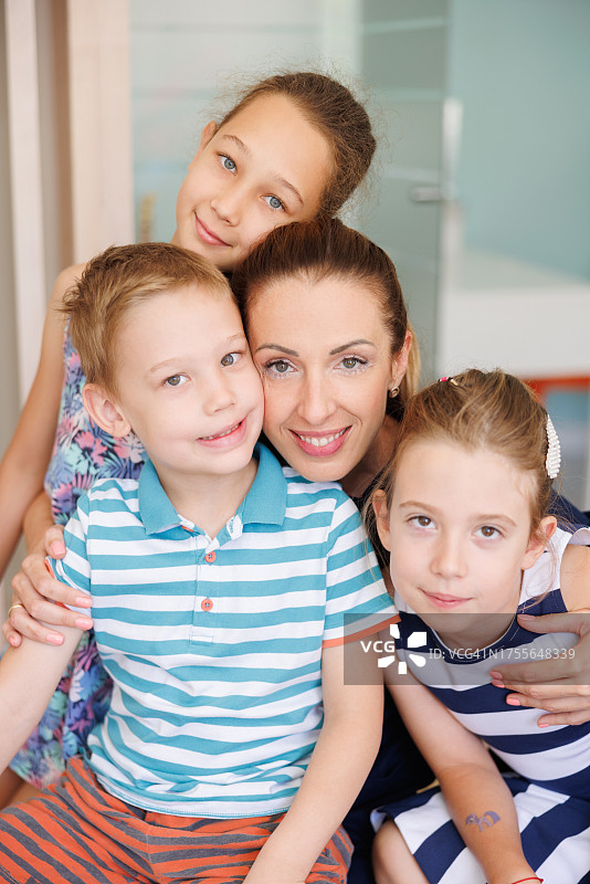 充满爱意的母亲对着镜头微笑，紧紧抱着她的三个孩子图片素材