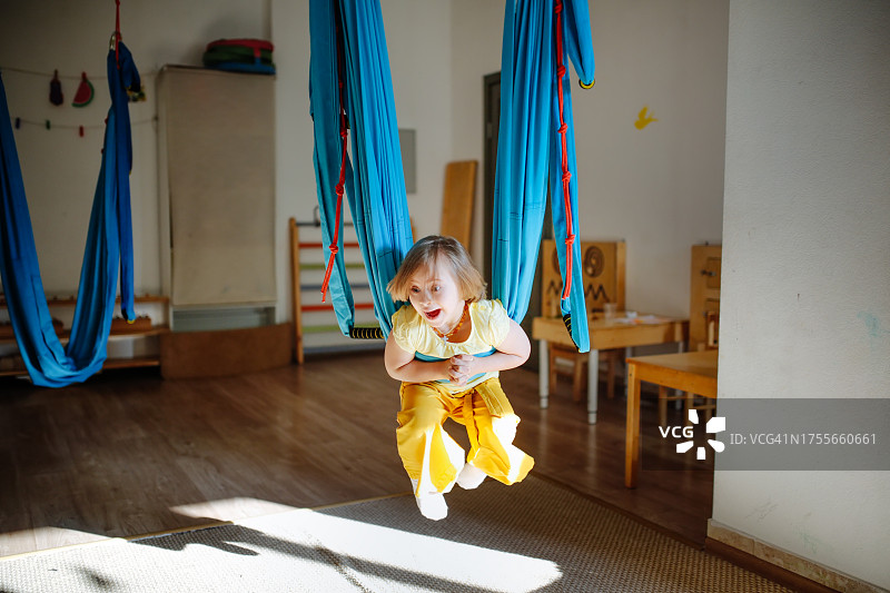患有唐氏综合征的快乐儿童穿着黄色衣服在吊床上荡秋千：空中瑜伽促进身体发育图片素材