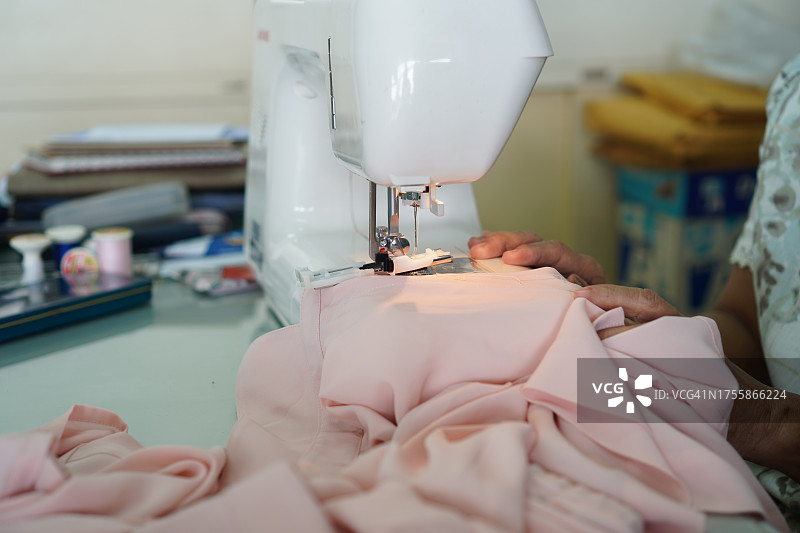 缝纫机特写：女士使用缝纫机缝制白色缎面连衣裙图片素材