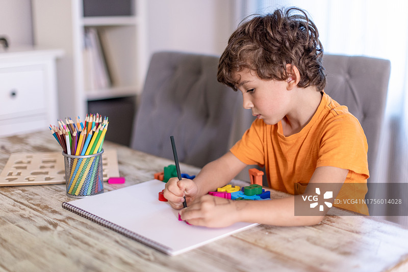 舒适的客厅氛围中，学龄前儿童和六岁卷发男孩沉浸在早晨的学习中，在餐桌上练习数字作业，周围环绕着木制数字辅助工具图片素材
