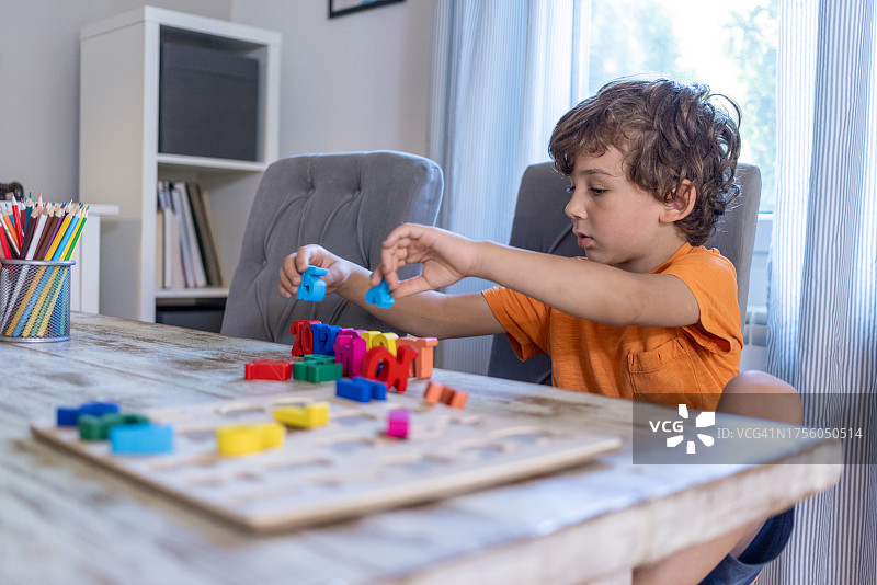 舒适的客厅氛围中,学龄前儿童和六岁卷发男孩沉浸在早晨的学习中,在餐桌上练习数字作业,周围环绕着木制数字辅助工具图片素材