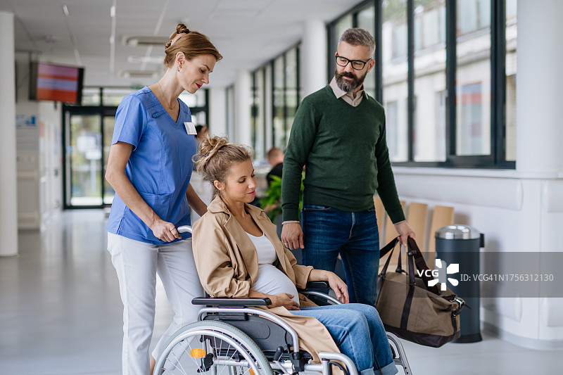 护士用轮椅送孕妇去妇产科病房，丈夫携带住院待产包图片素材