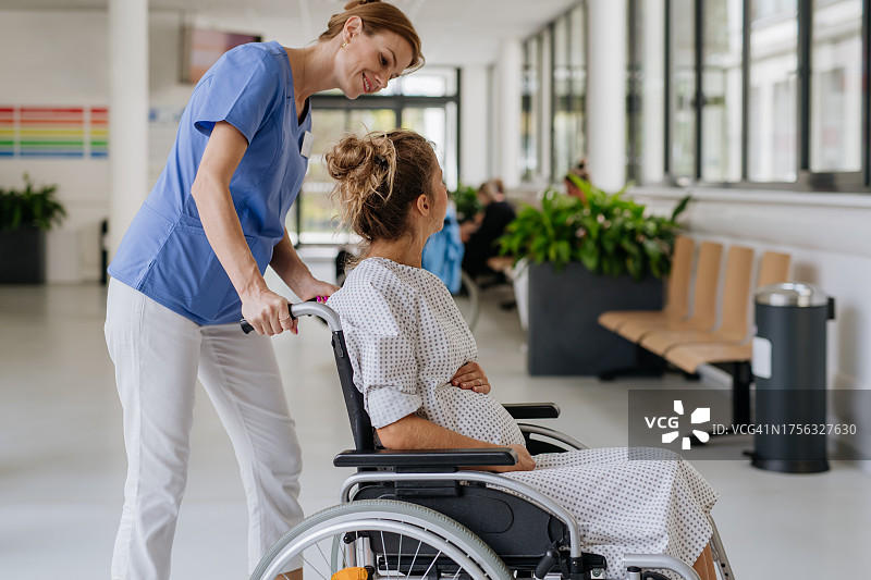 护士在医院用轮椅推送孕妇，产妇与助产士交谈图片素材