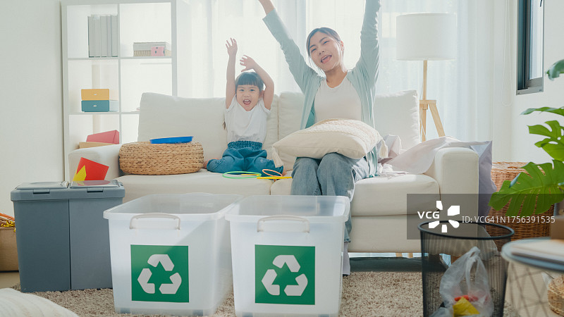 年轻的亚洲家庭妈妈教孩子如何回收利用，帮助女孩了解环保的重要性，在客厅里对着镜头微笑。家庭幸福时刻。图片素材