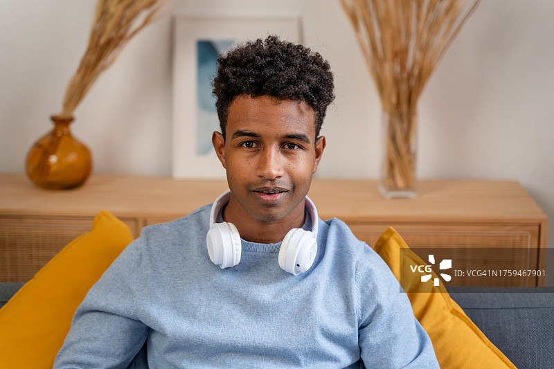 年轻的非裔美国男子戴着耳机坐在沙发上图片素材