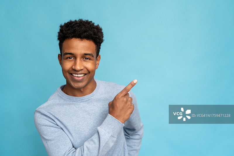 快乐的非裔美国男子指向蓝色背景上的文案区域图片素材