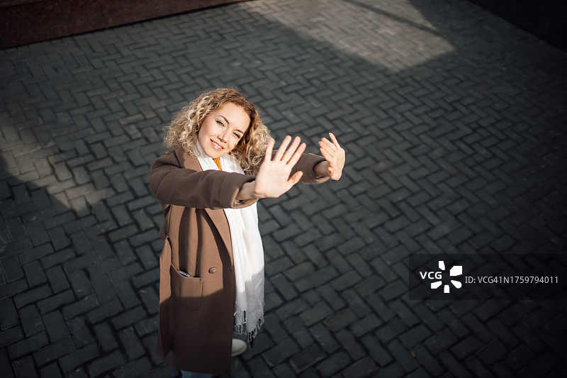 站在建筑物阴影中，双手举起迎接温暖秋日阳光的卷发美女高角度视图图片素材
