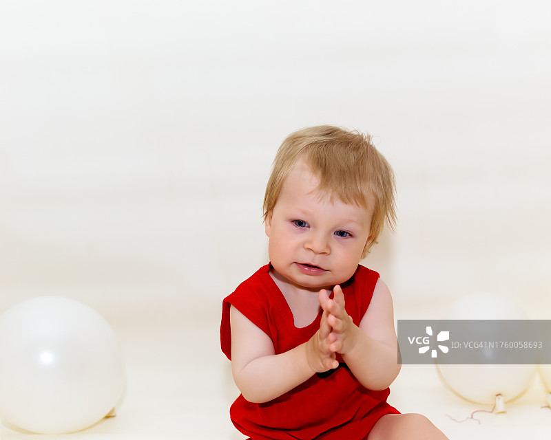 坐在白色背景前，拿着气球的可爱男孩图片素材