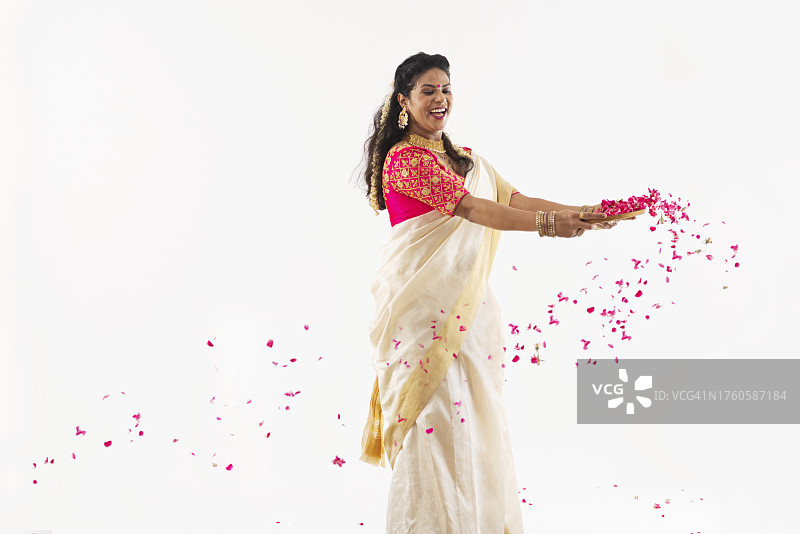 身着传统服饰，在纯色背景下吹着玫瑰花瓣的微笑女人图片素材