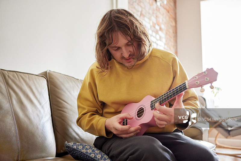 男人在家里的沙发上弹尤克里里图片素材