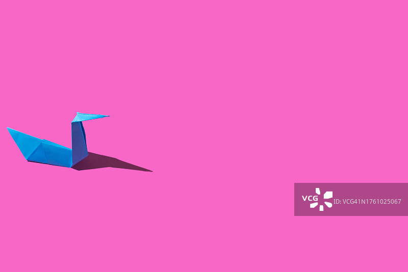 粉色背景上的蓝色纸天鹅折纸艺术概念图片素材