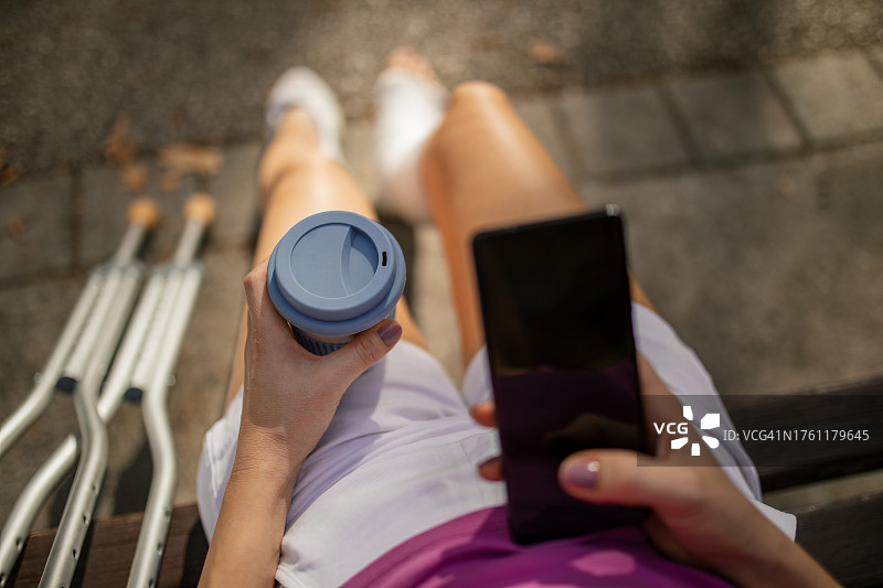 坐在公园长椅上、腿上打着石膏、使用手机的女人图片素材