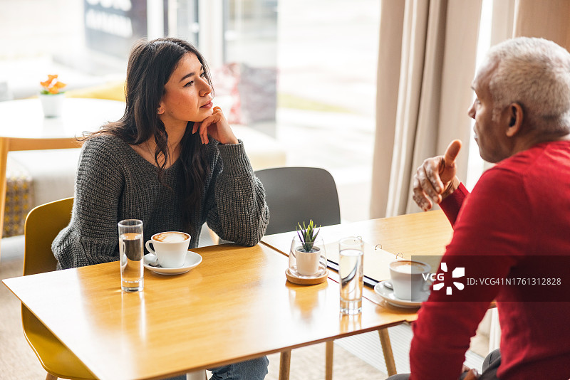 在舒适咖啡馆里交谈的白人女性和中年黑人男性图片素材