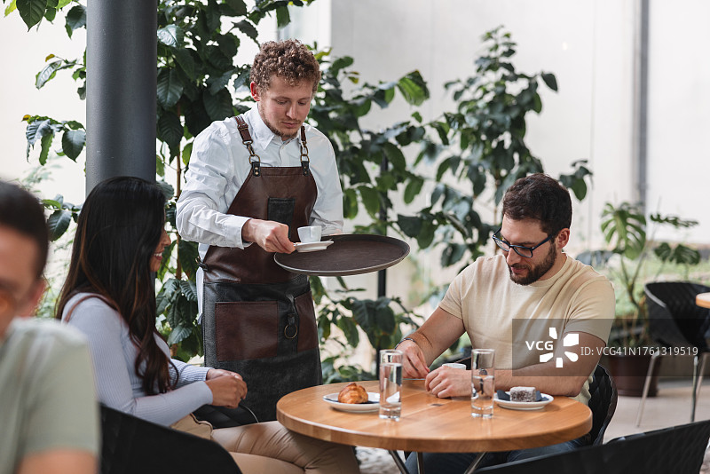 咖啡馆里的白人咖啡师为不同肤色的情侣提供咖啡图片素材