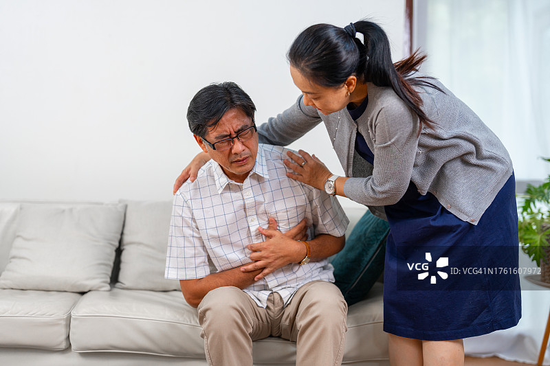 一位年长的男人在家里的沙发上感到胸痛。图片素材