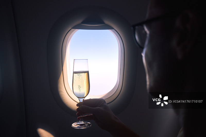 手持香槟酒杯，背景为飞机舷窗图片素材