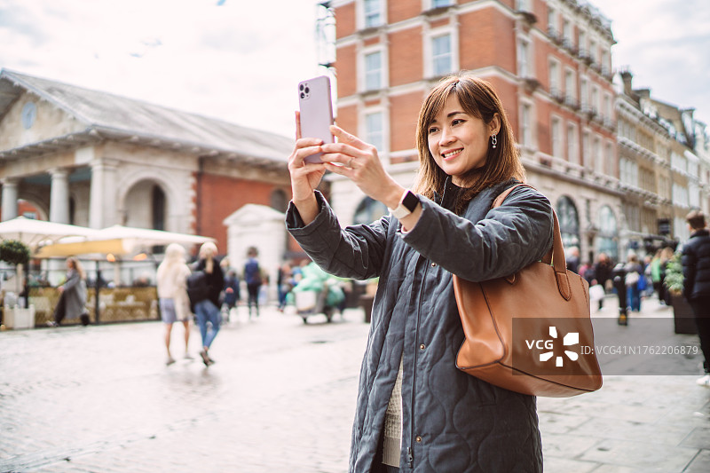 年轻漂亮的亚洲女性在伦敦市中心购物街用智能手机自拍图片素材